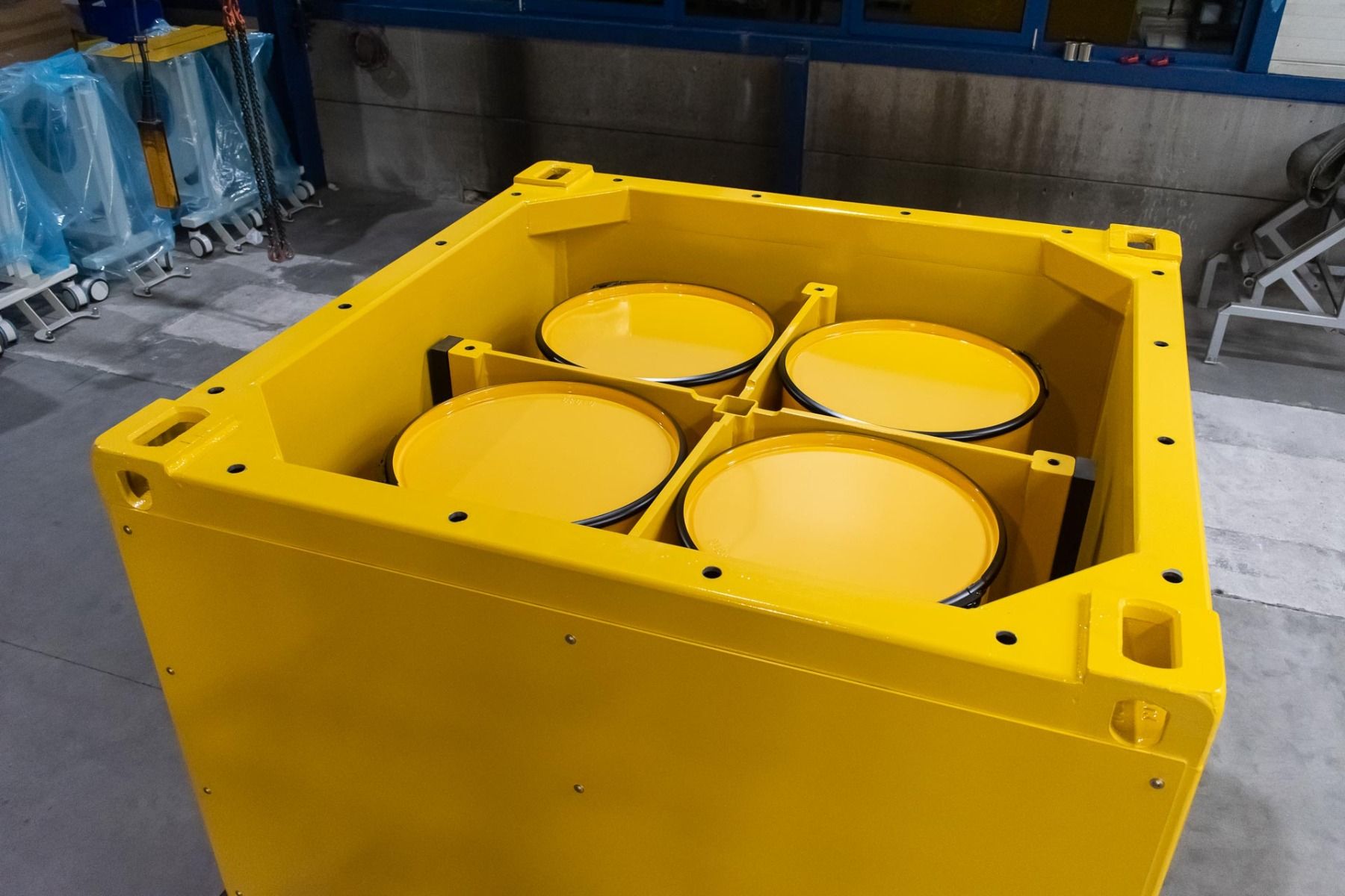 Yellow lead shielded cask containing four 200-litre drums, with crane lifting points and forklift pockets, in Nuclear Shields manufacturing facility